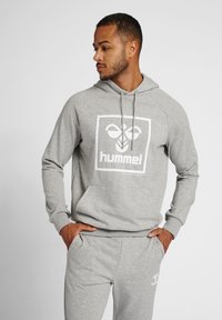 Grijze hoodie van zachte stof, met een groot wit logo in een vierkant, trekkoord bij de halslijn en geribbelde manchetten.
