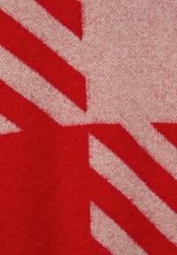 Nahaufnahme eines rot-weiß gestrickten Stoffes mit einem teilweise sichtbaren Union-Jack-Muster, das die detaillierte Textur und die Maschenarbeit zeigt.