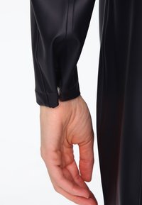 Black waterproof jacket sleeve with a smooth texture, featuring a button closure at the cuff and a fitted design. Hand positioned near the sleeve.