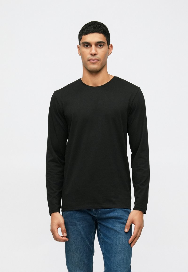 Μαύρο μπλουζάκι με μακριά μανίκια και στρογγυλή λαιμόκοψη, εφαρμοστό σχέδιο και απαλή υφή σαν βαμβάκι, συνδυασμένο με μπλε τζην παντελόνι.