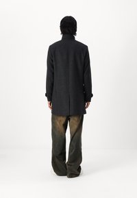 Grå ullfrakk med høy krage og lange ermer, kombinert med løse, falmede denimbukser. Enkelt design, ingen synlige dekorasjoner.