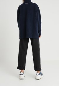 Marinblå oversized tröja med hög krage, texturerad stickad tyg och rullade ärmar, kombinerat med svarta, löst sittande byxor och vita sneakers.