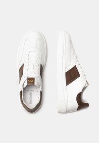 Sneaker in pelle bianca con accenti marroni, pannelli laterali testurizzati, lacci piatti e suola ammortizzata. Presenta il logo sulla linguetta.