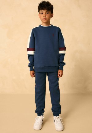 Dunkelblaues Sweatshirt und Jogginghose Set mit weißen und burgunderroten Streifen, aus weichem Material mit gerippten Bündchen. Mit Logo-Detail auf der Brust.