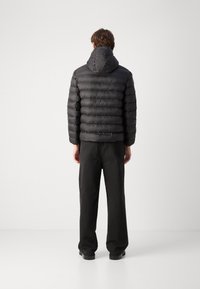 Giubbotto invernale nero con cappuccio, caratterizzato da un design trapuntato e un orlo corto. Abbinato a pantaloni neri, visto da dietro su uno sfondo bianco.