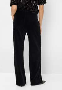 Zwarte corduroy wijde broek met een gestructureerde afwerking, voorzien van een hoge taille en lichte flare aan de onderkant, gedragen met een pailletten top.