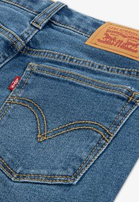 Blå denimtyg med en hjärtformad söm på bakfickan, förstärkta sömmar och en brun läderpatch med varumärket i midjan.