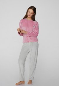 Camiseta rosa de felpa de manga larga con un pequeño lazo decorativo, combinada con pantalones a rayas gris claro con cinturilla elástica y cordón.