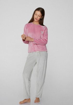 Rosa Plüsch-Langarmshirt mit einer kleinen dekorativen Schleife, kombiniert mit hellgrauen, gestreiften Hosen mit elastischem Bund und Kordelzug.