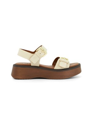 Des sandales platformes avec un dessus synthétique crème, deux boucles carrées et une semelle compensée imitation bois marron clair pour plus de hauteur.
