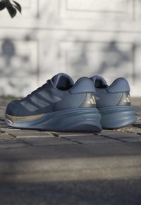 Blue athletic shoes with a textured upper, three stripe design, cushioned sole, and gold accents. Lightweight with a rounded shape.