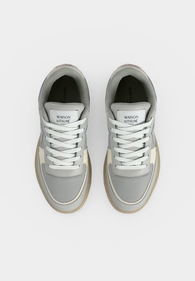 Ζευγάρι γκρι και άσπρα sneakers Maison Kitsuné με λευκά κορδόνια, από πάνω σε μονόχρωμο φόντο.