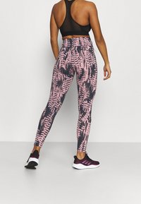 Legginsy z wysokim stanem, zdobione różowo-czarnym abstrakcyjnym wzorem, wykonane z elastycznego materiału. Zestawione z czarnymi butami sportowymi.