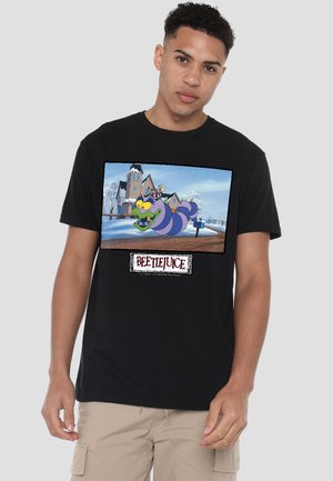 Young man wearing black T-shirt with colorful animated purple caterpillar and snowy house background, "Beetlejuice" text below.