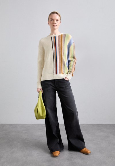 Knit sweater in cream with vertical multicolored stripes; paired with black wide-leg jeans and a green bag; brown shoes complete the outfit.
