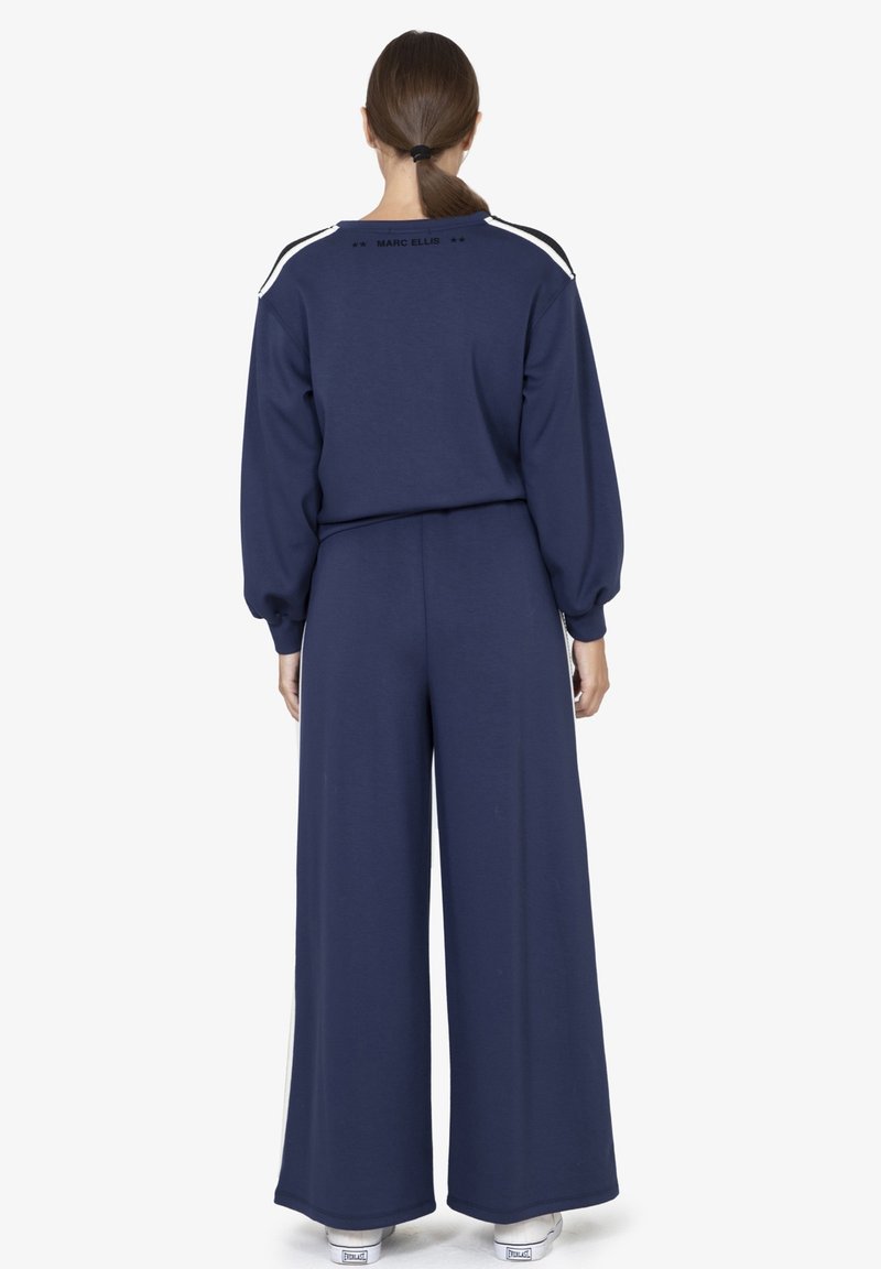 Pantaloni della tuta blu navy con cintura elastica e felpa coordinata blu navy con strisce bianche sulle spalle e logo sul retro.