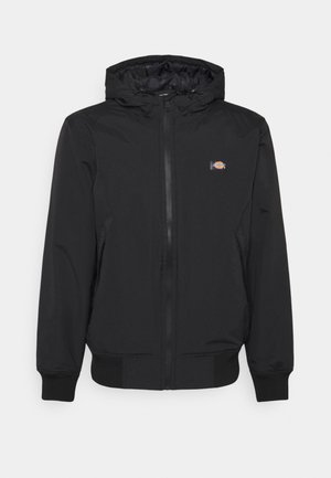 Black hooded jacket with zip closure, elastic cuffs, and hem. Features a small logo on the left chest. Smooth, lightweight fabric.