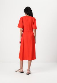 Rochie midi roșie cu mâneci scurte tip puff, talie strânsă și fustă fluidă. Purtați cu sandale bej cu curele. Textură de țesătură netedă.