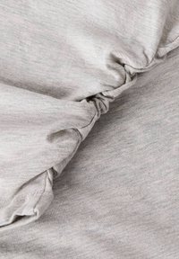 Tejido gris claro con una textura suave, que presenta detalles fruncidos. El material es elástico y tiene un patrón ligeramente jaspeado.