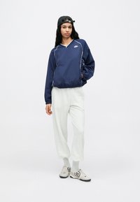 Sötétkék szélkabát fehér szegéllyel, könnyű anyagból, V-nyakú kialakítás, világosszürke nadrággal és szürke-fekete cipővel párosítva.