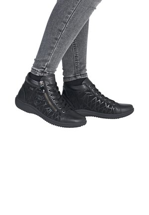 Baskets montantes noires avec un design en cuir texturé, fermeture éclair latérale et motif géométrique, associées à un jean skinny gris.