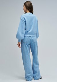 Suéter azul claro, texturizado, con mangas globo, combinado con jeans de tiro alto y pierna ancha de lavado claro. Diseño simple y casual.