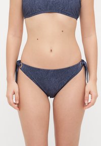 Denim-look bikini broekjes in donkerblauw met strikzijden en metallic hardware accenten. Zachte textuur en een ontwerp met gemiddelde bedekking.
