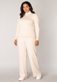 Beige coltrui gecombineerd met beige wijde broek, gemaakt van zachte stof. Gedragen met witte sneakers voor een casual uitstraling.