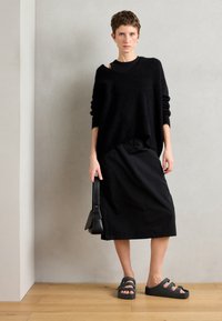 Zwarte oversized fuzzy trui laag over een zwart top, gecombineerd met een zwarte rok tot de knie en chunky zwarte sandalen. Kleine zwarte handtas.