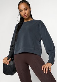 Felpa corta grigio scuro con maniche lunghe, caratterizzata da un logo sottile e dettagli cuciti, abbinata a leggings marroni a costine testurizzati.