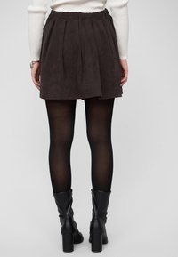 Falda de pana marrón oscuro con pliegues, cintura elástica, combinada con medias negras y botas negras de tacón. La textura parece suave y acanalada.