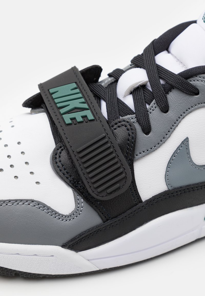 Baskets blanches et grises avec des accents noirs, dotées d'une sangle en caoutchouc étiquetée "NIKE", cuir texturé et design à lacets.