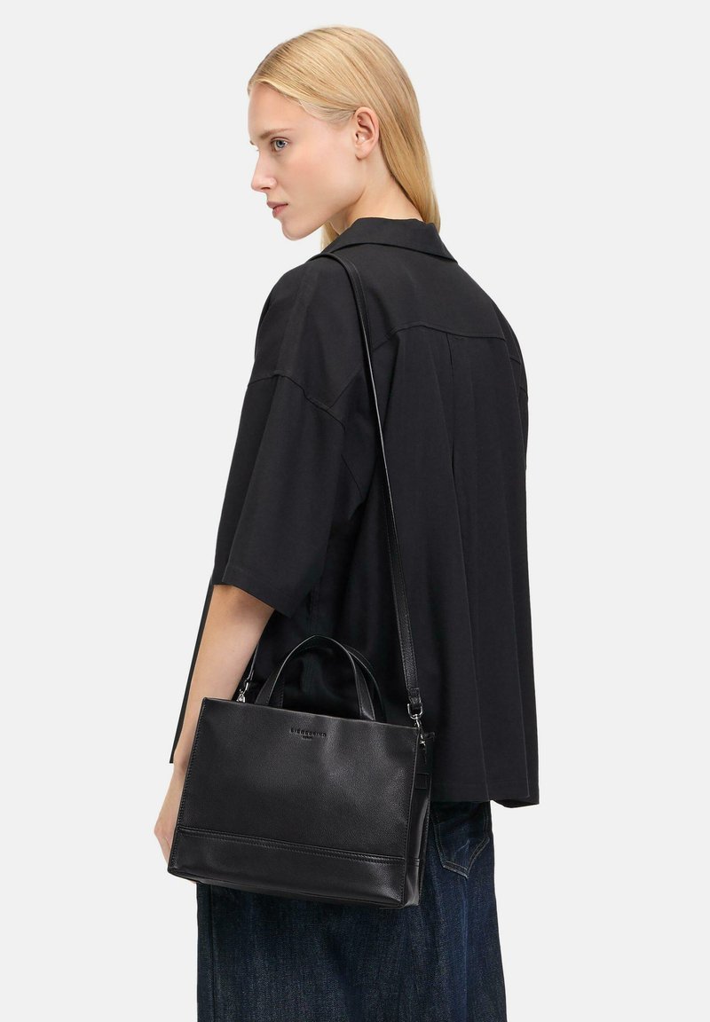Sac à main en cuir noir avec une poignée supérieure et une bandoulière ajustable. Présente une finition texturée et un logo discret à l'avant.