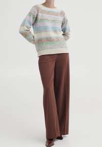 Trui van zacht, meerkleurig garen met horizontale strepen in pastelkleuren; gecombineerd met een broek met hoge taille in bruin en puntige bruine schoenen.