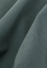 Prim-plan al unui material textil plisat de culoare verde închis, evidențiind textura și finele linii diagonale.