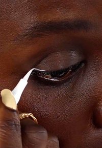 Hvit eyeliner penn påføres det øvre øyelokket på mørk hud, noe som fremhever den naturlige øyeformen; nærbilde som viser fine detaljer og tekstur.