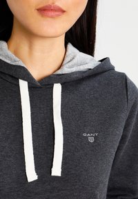 Grijze katoenen hoodie met een lichtgrijze voering, voorzien van witte trekkoorden en een klein GANT-logo op de borst.