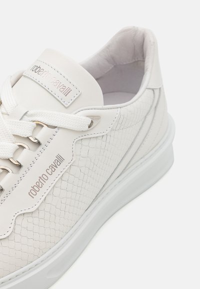 Fehér sneaker érdes, domború bőrből, fűzős kialakítással, logóval ellátott nyelvvel és gumitalppal. Fém fűzőlyukakkal és diszkrét varrással rendelkezik.