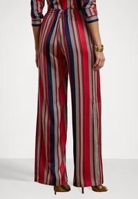 Wide-leg trousers made of smooth fabric featuring vertical stripes in red, navy, and cream, with an elastic waistband and a relaxed fit.