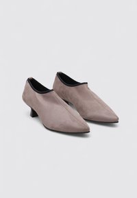 Botas de tobillo de ante en gris claro, con punta afilada, tacón bajo y forro negro. Textura suave con un detalle de costura mínimo.