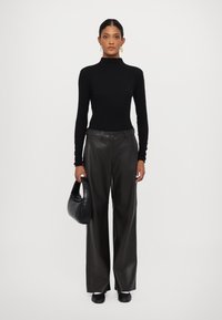 Fitted svart turtleneck, høyt liv mørke skinn vide bukser og en svart håndveske, iført med flate svarte sko.