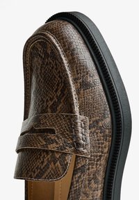 Mocassino marrone a motivo serpente realizzato in pelle texturizzata con suola in gomma nera. Presenta un dettaglio cucito e un design classico da penny loafer.