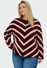 Maglione a righe bordeaux e crema con motivo a zig zag, scollatura a girocollo, vestibilità ampia e texture morbida, abbinato a jeans blu.