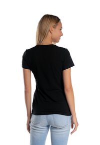 Czarny t-shirt z krótkim rękawem wykonany z bawełny, o luźnym kroju i okrągłym dekolcie, pokazany z tyłu w zestawieniu z jasnoniebieskimi dżinsami.