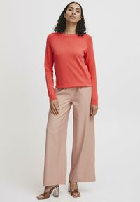 Maglione corallo a maniche lunghe abbinato a pantaloni palazzo rosa chiaro. Sandali con tacco trasparente completano l'outfit. Design semplice e moderno.