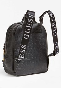 Sac à dos noir avec un motif de logo en relief, des compartiments zippés et des sangles noires ajustables portant la marque "GUESS" en blanc. Matériau lisse.
