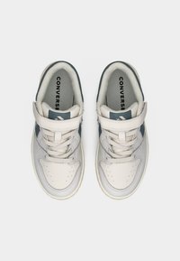 Ζευγάρι λευκά και γκρι παπούτσια Converse με κορδόνια και λουράκια με βέλκρο, σε θέα από ψηλά πάνω σε απλό φόντο.