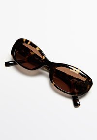 Occhiali da sole tartarugati con un design elegante e oversize. Lenti marrone sfumato e montatura spessa e lucida. Materiale plastico resistente.