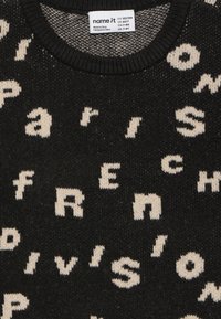 Schwarzer Strickpullover mit cremefarbenen Buchstaben, die "Paris" und "French Division" in einem sich wiederholenden Muster über den Stoff spell.
