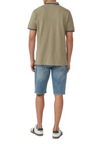 Oliwkowa koszulka polo z czarno-białym paskowanym kołnierzykiem, zestawiona z jasnoniebieskimi szortami dżinsowymi. Casualowe obuwie dopełnia stylizację.